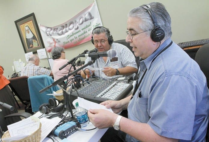 Volunteer Cucho Garcia, foreground, of St. Benedict Church, Johns Creek, and German Medina, background right, of Our Lady of the Americas Church, Lilburn, take turns reading pledges over the airwaves during the second radio marathon for the Spanish Catholic radio program, “Nuestra Fe” (Our Faith), April 18.