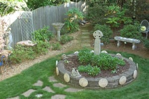 A Celtic cross sits in the center of a bed of Shasta daisies. On the top of the wall surrounding the bed is a statue of the Nativity. The circular stones surrounding its base are Stations of the Cross, made by the late Cistercian monk Father Bob Pearson.(Photo By Michael Alexander)