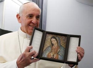 Pope holds image of Our Lady of Guadalupe after receiving gift from journalist aboard papal flight to Brazil.