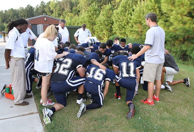 Jack Murray, standing right, area director for Fellowship of Christian Athletes, leads the Monsignor Donovan Rams in a prayer just before their season opener against Nathanael Greene Academy of Siloam.