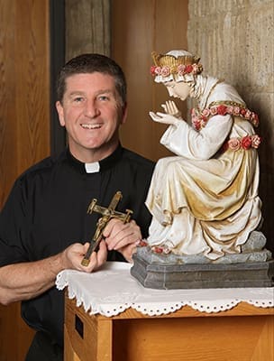 Standing in the church narthex, La Salette Father Brian Sheridan, pastor of St. Thomas the Apostle Church, Smyrna, holds a La Salette crucifix as he stands beside a statue of Our Lady of La Salette. On the right side of the crucifix is a hammer, which represents the sinfulness of humanity that nailed and continues to nail Jesus to the cross. The pincer on the left side of the crucifix represents our reconciliation to Jesus. Photo By Michael Alexander