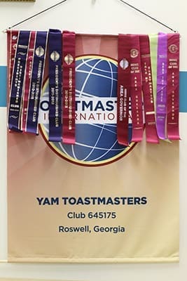 A banner, draped with ribbons, hangs in the YAM Toastmasters Club meeting room at St. Andrew Church in Roswell. The ribbons signify various distinctions earned by the club over the years. They also recognize achievement in club education and leadership goals, membership growth, and service by club members as district officers. The club is celebrating its 10th anniversary of existence. Photo By Michael Alexander