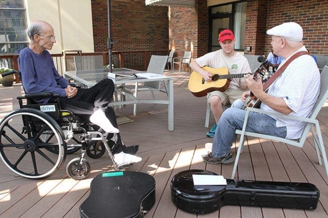 (Clockwise, from left) Phillip Maloney sits on the back deck of Our Lady of Perpetual Help Home as his son, Ben, and Ben’s music instructor, Jim “Duck” Adkins, stop by to perform some bluegrass tunes the weekend of Father’s Day. The elder Maloney is a parishioner at St. Joseph Church, Marietta. Photo By Michael Alexander