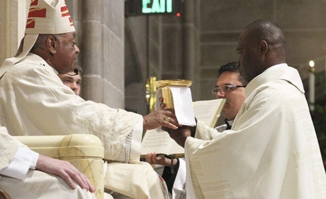 Archbishop Wilton D. Gregory, left, presents the chalice and paten to newly ordained Father Junot Nelvy as a sign of his office. Photo By Michael Alexander
