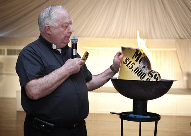 Msgr. Edward Dillon burns the mortgage, retiring the debt incurred from the parish’s capital campaign project, during the June 8 parish picnic on Pentecost Sunday at Holy Spirit Church. Msgr. Dillon became the full-time pastor of the parish in 1987. 
