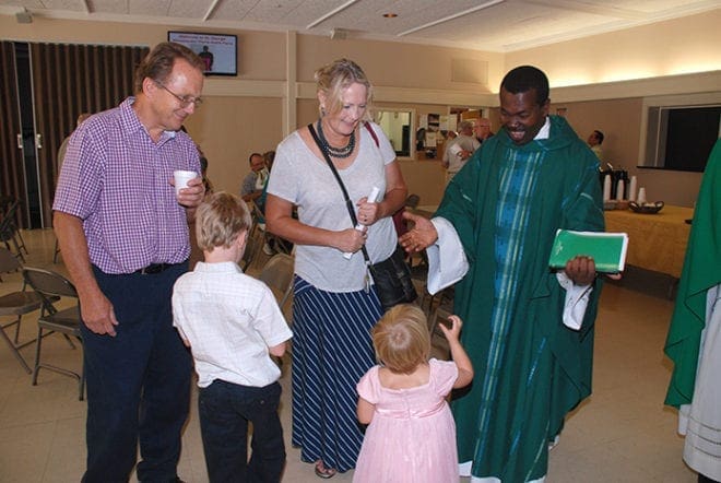 St. George parishioners Joe and Connie Cebulski with grandchildren, Silas and Lula, greet Msgr. André Pierre of Haiti following Mass July 26. He shared his tale of having lived through the devastating 2010 earthquake there and how education will help the country move forward. Photo by Debby Dye