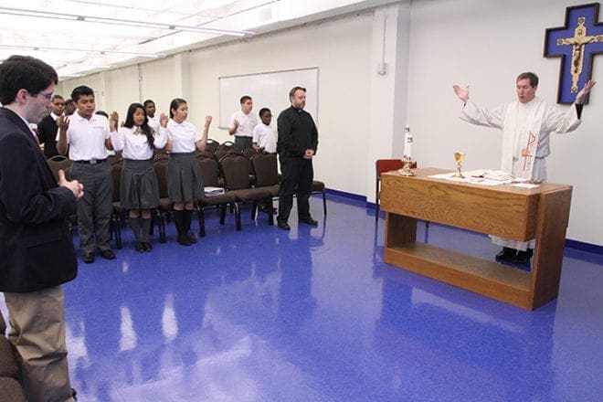 Bethy Ramirez-Sanchez, third from the left, joins some of her classmates during morning Mass at the school. Jesuit Father James Van Dyke, far right, principal of Cristo Rey Atlanta Jesuit High School, is the liturgy’s main celebrant. Photo By Michael Alexander