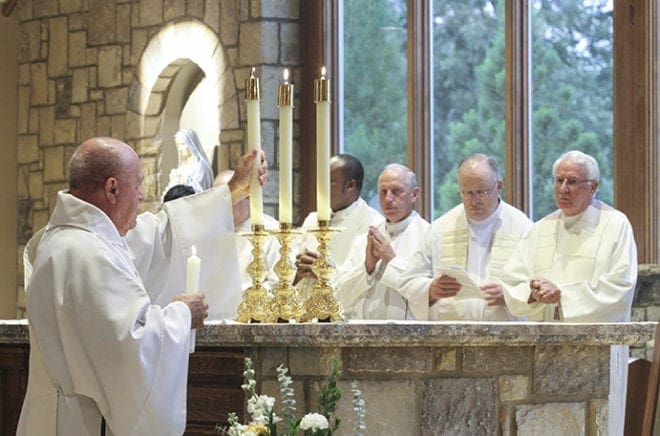 After the anointing and censing of the altar, Deacon Donald Nadeau lights the candles on the altar. In the background are the priests concelebrating with the archbishop, including (r-l) Father Francis X. Richardson, pastor of Good Shepherd Church, Msgr. Dan Stack, pastor of St. Thomas Aquinas Church, Alpharetta, Legionaries of Christ Father Matthew Van Smoorenburg, pastor of St. Brendan the Navigator Church, Cumming, and Father Michael Onyekuru, pastor of St. John Evangelist Church, Hapeville. Photo By Michael Alexander
