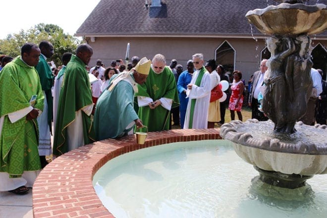 Archbishop Wilton D. Gregory pulls water from the fountain in Christ Our Hope's new memorial garden. The entire grounds of the church constitute a meditation garden, with statues of Mary and Joseph and Stations of the Cross. A rosary garden will be constructed around the fountain. Photo By Byron Henry