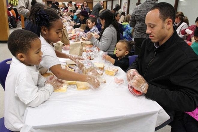 (Clockwise from top left) Dallis Welsh, a St. John the Evangelist School second-grader, 2-year-old Jordyn Daniels, her father John and his 5-year-old son Chase join a multitude of others as they make sandwiches with lunchmeat and cheese for the homeless. Photo By Michael Alexander