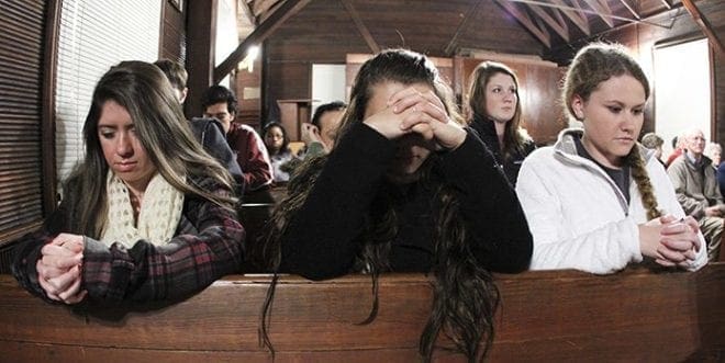 University of West Georgia freshmen (l-r) Brittany Ricciardi, Caitlin Teknipp and Theresa Daugherty kneel in silent prayer before the Nov. 17 Mass begins at the school’s Kennedy Chapel. The chapel was moved to the campus 50 years ago, donated by the Catholic church. Photo By Michael Alexander