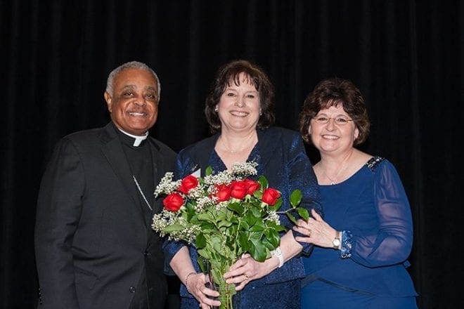 Flanked by Archbishop Wilton D. Gregory, left, and Diane Starkovich, Ph.D., superintendent of Catholic schools for the Archdiocese of Atlanta, Lauren Schell poses with flowers to celebrate the honor of being named principal of the year. Schell has served as principal of Holy Redeemer School, Johns Creek, for five years. She was a founding teacher there when the school opened in 1999. Photo By Thomas Spink