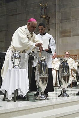 Archbishop Wilton D. Gregory, left, stirs the chrism as seminarian Avery Daniel looks on during the March 31 Chrism Mass at the Cathedral of Christ the King, Atlanta. Photo By Michael Alexander