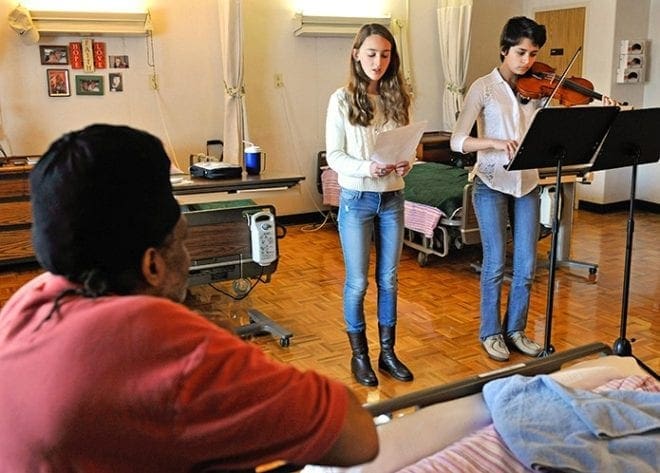 Students Mary Margaret Cozart, 14, of St. Pius X High School, and Michaela Pocock, 17, of Roswell High School, perform for Anthony Carmouche at Our Lady of Perpetual Help Home. Photo By Lee Depkin