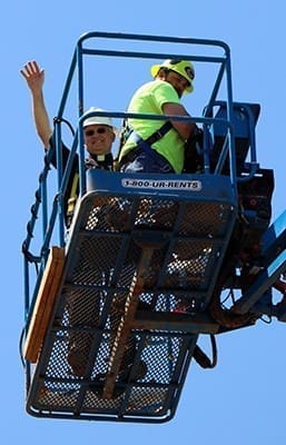 Father Larry Niese, pastor of St. Michael the Archangel Church, in Woodstock, waves to the crowd from a lift where he was taken on Good Friday to bless the new church steeple. The parish is building a new church that will be dedicated Aug. 29.