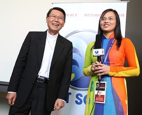 Bishop Peter Kham Van Nguyen, left, of the My Tho Diocese in Vietnam, concludes an interview with Viet Sóng Media’s Kim Ngan outside the Vietnamese track in the Marriott Gateway hotel. Photo By Michael Alexander
