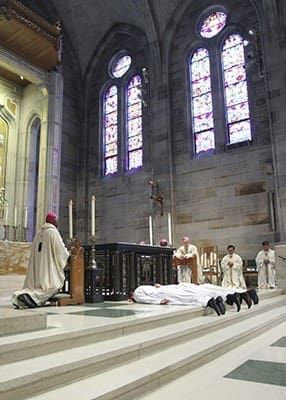 Ordination candidates (l-r) Roberto Suárez Barbosa, Carlos Cifuentes and Valery Akoh prostrate themselves before the altar of the Lord at the Cathedral of Christ the King, Atlanta, during the litany of supplication. Photo By Michael Alexander