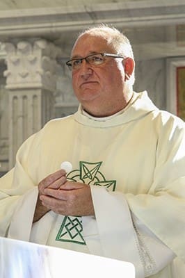 Father Paul Flood, pastor of St. Benedict Church, Johns Creek, stands at the altar as he holds the Body of Christ. The Dublin, Ireland, native was ordained on June 10, 1990, at Dublin’s All Hallows Missionary College. His first assignment in the Archdiocese of Atlanta was at Corpus Christi Church in Stone Mountain. Photo By Michael Alexander