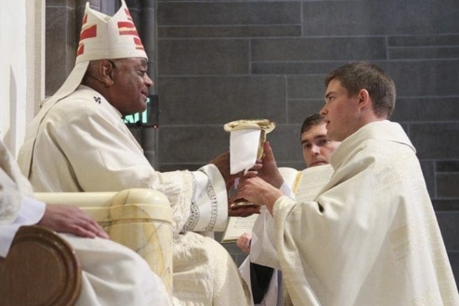 Archbishop Wilton D. Gregory, left, presents the chalice and paten, a sign of the new priest's office, to Father Branson Hipp. Father Hipp will assume his first assignment as parochial vicar at St. Patrick Church, Norcross. Photo By Michael Alexander