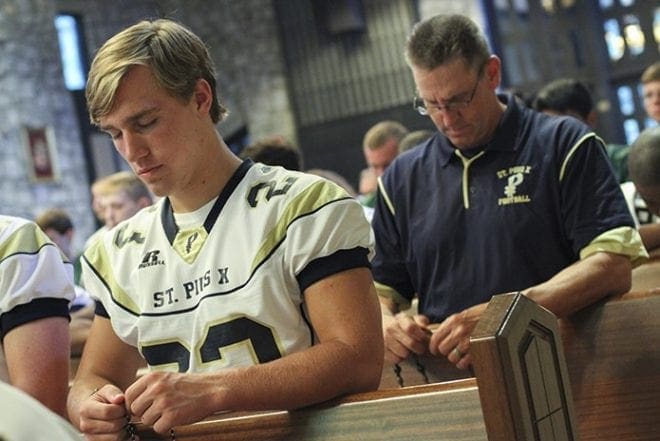 St. Pius X High School senior wide receiver and safety Griffin Thomas, foreground, and tight ends coach and special teams coordinator Bob Gilbert, background, pray the rosary with fellow football players and coaches. Sports Leader of Louisville, Ky., a virtue-based mentoring and motivation program for coaches and student athletes, sponsored the Aug. 5 rosary rally. Photo By Michael Alexander