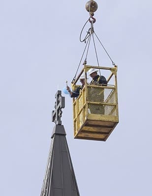 Accompanied by parochial vicar Father Fausto Marquez, Father Dan Fleming, pastor of St. Andrew Church, sprinkles the four-foot cross atop the cupula with holy water on Aug. 19. Photo By Michael Alexander