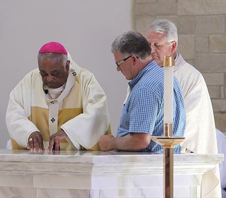 Archbishop Wilton D. Gregory places relics of St. John Neumann and St. Elizabeth Ann Seton in the altar. Looking on are Father Larry Niese, far right, and his brother Ron, one of eight relatives from Ohio who drove down for the dedication. Photo By Michael Alexander