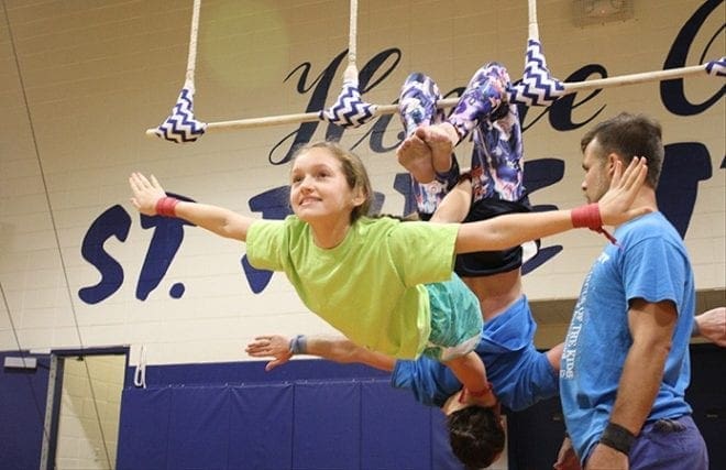 St. Jude the Apostle School seventh-grader Mary Beth Fason practices the trapeze with instructors James Finch, standing right, and Joe Gallogly, background, hanging from trapeze. Photo By Michael Alexander