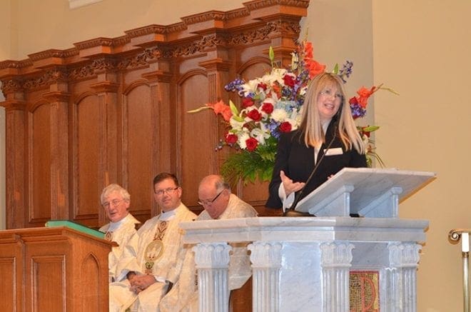 Sally Kazin, director of the Marian Servants of the Blessed Trinity, speaks during Mass Sept. 10 at St. Benedict Church, Johns Creek, where four people were received as full members and nine others as candidates. Seated, left to right, are Msgr. Hugh Marren, Father Tim Hepburn and Father Paul Flood, concelebrants of the Mass. 