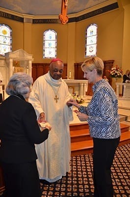 Archbishop Wilton D. Gregory gives the rule of life for the Marian Servants to Pat Thernell, right, a St. Benedict parishioner and one of nine people beginning as candidates. Diane Brown, left, founded the Marian Servants in Clearwater, Florida. There are now 14 U.S. communities. Photo by Cindy Connell Palmer