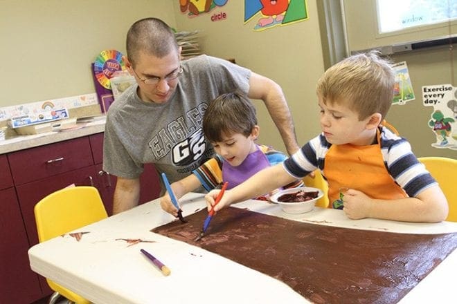 (L-r) Erik Kepshire volunteers in the prekindergarten class with his 4-year-old son Luke and 5-year-old J.T. Melton as they jointly paint the trunk of a tree. Photo By Michael Alexander