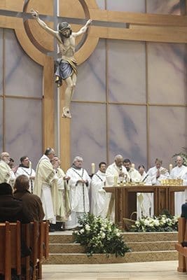 Archbishop Wilton D. Gregory, center, stands before the altar among his fellow clergy during the Lamb of God prayer. The new reredos with the corpus of Jesus looming above the altar provides a dominant visual presence. Photo By Michael Alexander