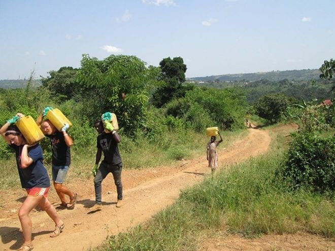 Regina Cothren and Stephen Smith of To the Nations lead the way with water jugs to a building site near Masaka, Uganda.