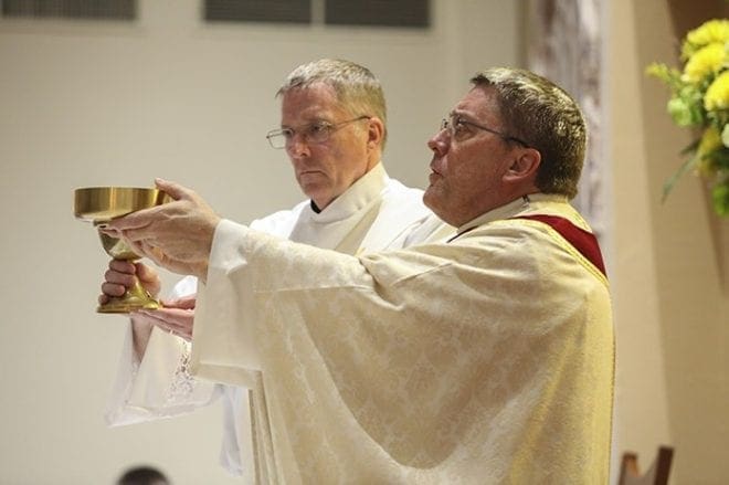 Father Mark Starr, right, and Deacon Thomas Ryan elevate the body and blood of Christ, respectively, during the Great Amen of the March 26 Easter Vigil Mass at St. Clare of Assisi Mission, Acworth. Father Starr serves as the administrator of the mission, which started in the summer of 2014. Photo By Michael Alexander