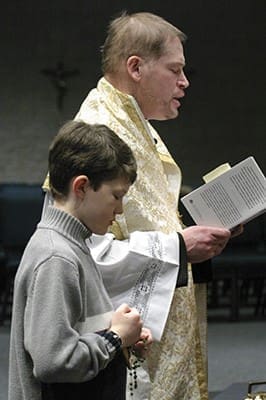 Nine-year-old Patrick Manyak joins Father Joseph Peek at the altar during the joyful mysteries of the rosary, which preceded the Communion of Reparation Vigil Mass at St. Peter Chanel Church, Roswell. The service was sponsored by the Alliance of Two Hearts, Georgia, in March 2005. Photo By Michael Alexander 