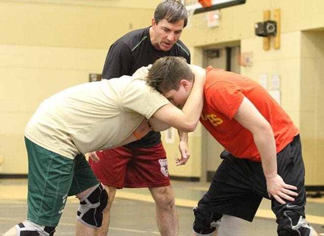 Assistant coach Mike Miller, center, observes as sophomore Sam Adams, left, and junior Colin Steinbach perform wrestling maneuvers on one another during practice. Photo By Michael Alexander