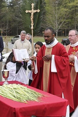 On Palm Sunday Father Gilbert Exumé, foreground, pastor of St. Matthew Church, Winder, blesses the palms as Deacon Larry Welsh, background right, and the altar servers stand before the congregation gathered in front of the church. Photo By Michael Alexander