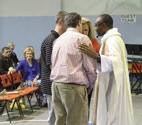 Gini Eagen, background left, exhibits some emotion as Claretian Father Paschal Amagba, pastor of Corpus Christi Church, Stone Mountain, prays with her children (clockwise, from left) Daniel, Jeff and Lisa after they brought up the offertory gifts. Photo By Michael Alexander