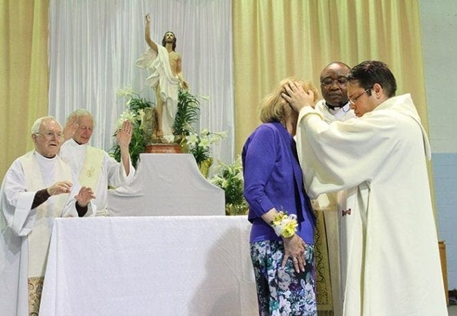 Claretian Fathers Paschal Amagba, foreground center, pastor of Corpus Christi Church, Stone Mountain, and Alex Gaitan, foreground right, associate pastor, extend a special blessing over Gini Eagen at the close of the Mass of thanksgiving in her honor. In the background pastor emeritus Claretian Father Greg Kenny, left, and Deacon Ken Melvin extend their hands toward Eagen, along with the entire congregation, during the blessing. Photo By Michael Alexander