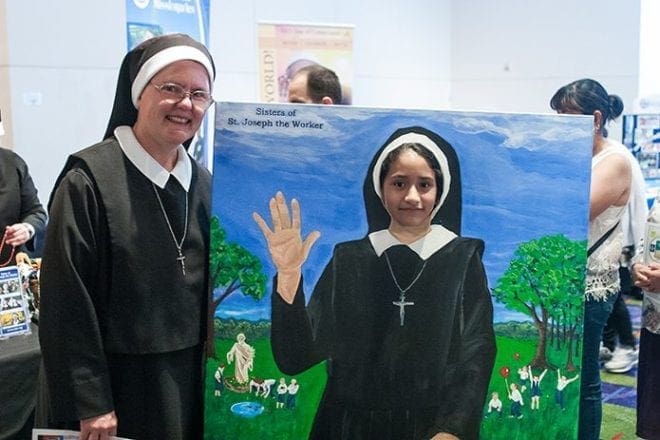 A number of religious communities hosted booths in the main hallway at the 2016 Eucharistic Congress in Atlanta, so they could share information about their work and ministry. Sister of St. Joseph the Worker Patricia Jean, of Walton, Kentucky, helped Jenny Gonzalez, age 9, from Good Shepherd Church, Cumming, “try on” a habit. Photo By Thomas Spink