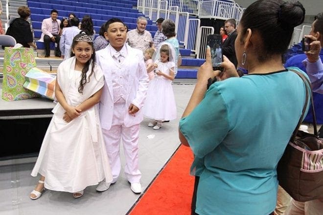 Following the Mass where they made their first Communion, 9-year-old Mary Carmen Quiroga and her 12-year-old brother, Francisco, pose for a photograph as their mother, Benita Gonzalez, captures it on her smartphone. Photo By Michael Alexander