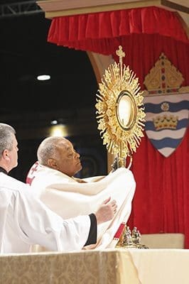 With assistance from Deacon Thomas McGivney of St. Thomas Aquinas Church, Alpharetta, left, Archbishop Wilton D. Gregory removes the monstrance containing the Blessed Sacrament from its stand during Benediction at the Eucharistic Congress June 4. Photo By Michael Alexander