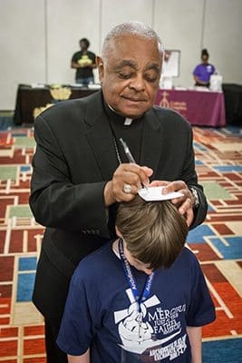 Archbishop Wilton D. Gregory uses the head of a young autograph seeker to sign his name during day two of the Eucharistic Congress. Photo By Thomas Spink