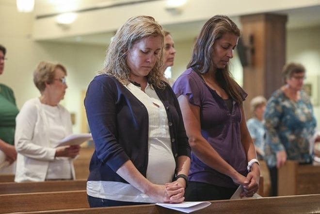 Vivian Cook, left, and Veena Black stand with the rest of the congregation as pastor Msgr. Albert Jowdy conducts the opening prayer of the Vigil for Peace at Immaculate Heart of Mary Church, Atlanta. Photo by Michael Alexander