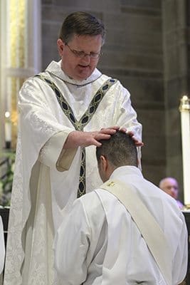 Msgr. Joe Corbett, pastor of St. Jude the Apostle Church, Sandy Springs, lays hands upon ordination candidate Roberto Suarez Barbosa during the June 25 rite of ordination to the priesthood. Father Barbosa’s first assignment as parochial vicar will be at St. Jude. Photo By Michael Alexander