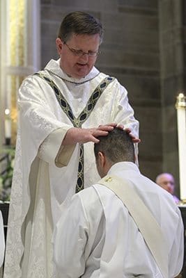 Msgr. Joe Corbett, pastor of St. Jude the Apostle Church, Sandy Springs, lays hands upon ordination candidate Roberto Suarez Barbosa during the June 25 rite of ordination to the priesthood. Father Barbosa’s first assignment as parochial vicar will be at St. Jude. Photo By Michael Alexander