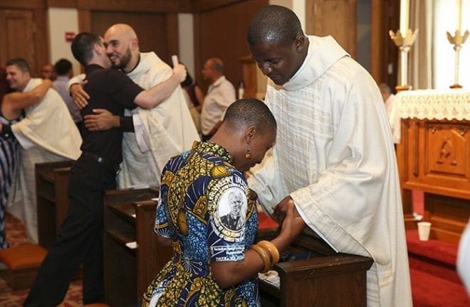 As his newly ordained brother priests in the background bless and greet others during the reception, Father Valery Akoh gives a blessing to Bibiana Tita, a family friend and fellow Cameroonian from St. Elizabeth Ann Seton Church in Delaware. Photo By Michael Alexander