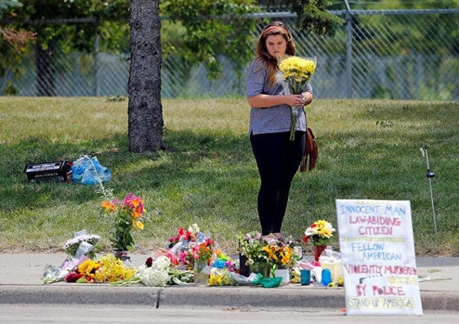 A woman brings flowers to a makeshift memorial July 7 at the site of the police shooting of Philando Castile in Falcon Heights, Minn. CNS Photo/Eric Miller, Reuters
