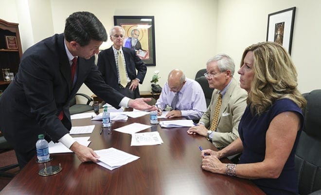 (L-r) Attorney at law Bradley C. Skidmore, foreground left, addresses the land purchaser Betsy Orr of the limited liability company Purification Properties, LLC, right, and William D. deGolian, chairman of The Friends of Purification Church, second from right. In the background attorney Andrew C. Shovers, left, looks on as John F. Schiavone, director of real estate development for the Archdiocese of Atlanta, signs a document. Skidmore’s firm represented Orr and Shovers’ firm represented the Archdiocese of Atlanta during the closing proceedings July 20. Photo By Michael Alexander
