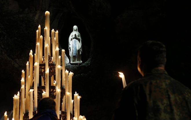 A military member holds a candle in front of the statue of Mary at the grotto at the Shrine of Our Lady of Lourdes in southwestern France May 17. CNS photo/Paul Haring 