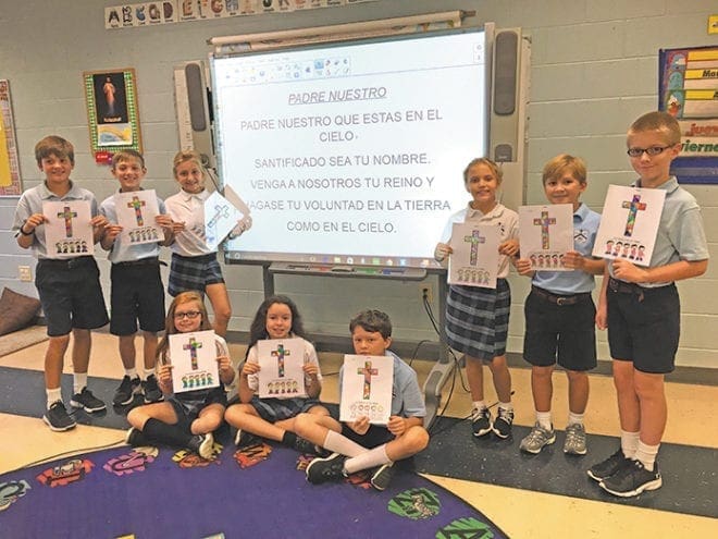 St. Mary’s School, Rome, fifth-grade students surround a projection of the Our Father in Spanish, which was prayed by the school on Friday, Sept. 9. Images of the cross were also colored by younger grades.